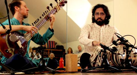 Image shows one muscian playing the sitar and another one playing the tabla. the 