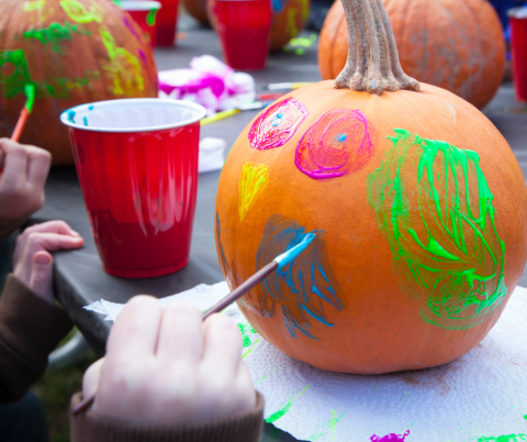 person painting a design on a small pumpkin