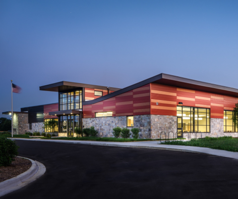 Exterior view of the front of the White Lake Township Library at night with the lights indoors turned on.