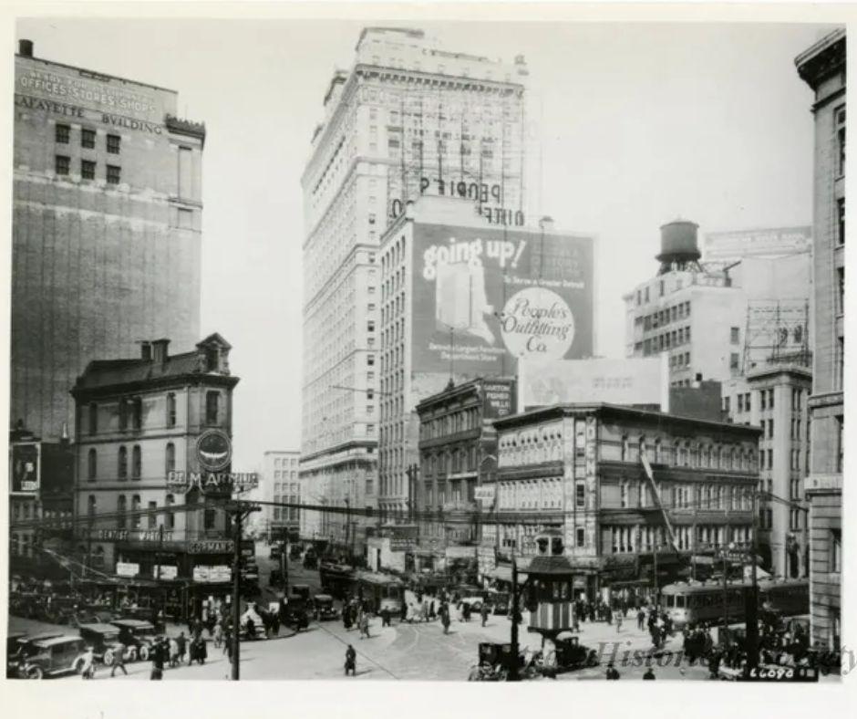 Detroit street in the 1920s with buildings, pedestrians, and billboards