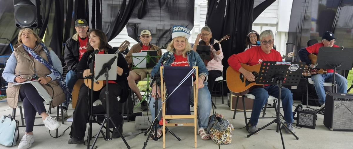 Photo of 9 band members sitting down on chairs with their instruments facing forward.